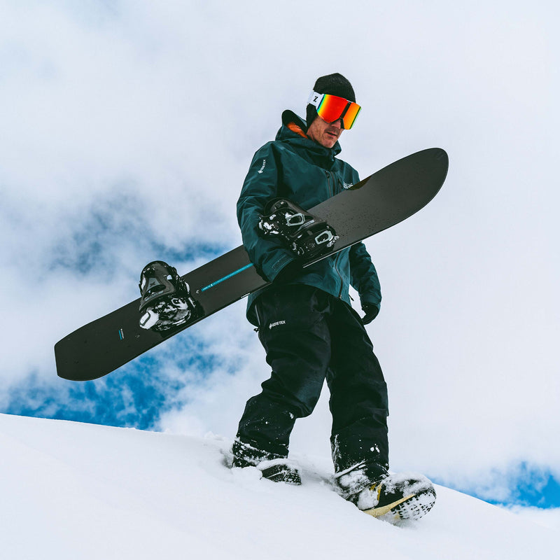 Freeride snowboarder walking with black and blue United Shapes Cadet board