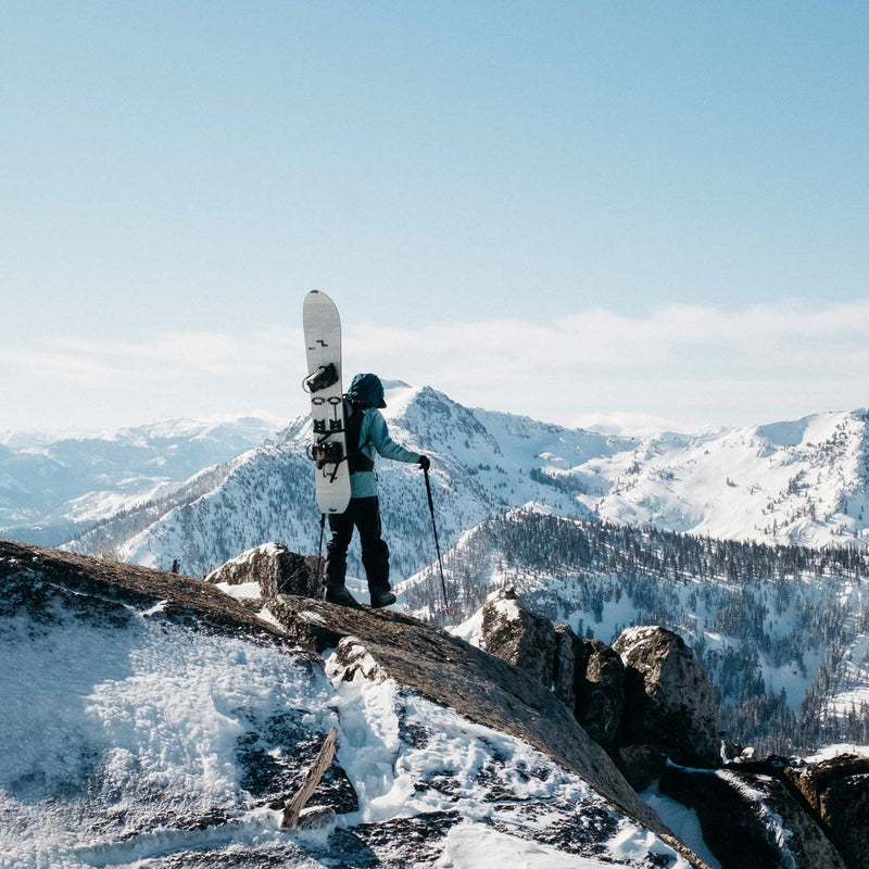 Snowboarder walking on mountain top with white splitboard Covert by United Shapes