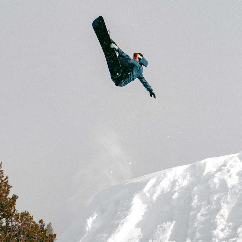 Snowboarder doing flip with United Shapes black Horizon board